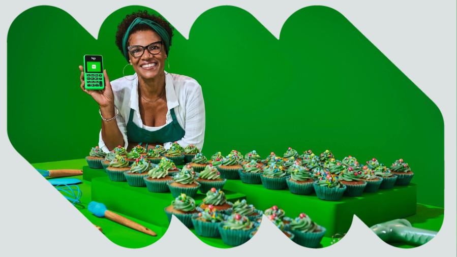 mulher atrás de uma mesa com cupcakes segurando maquininha de cartão