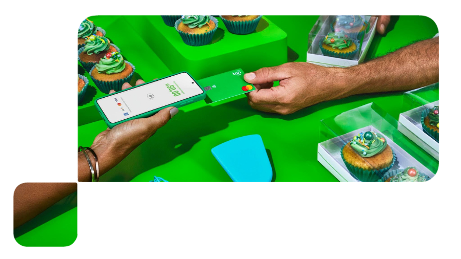 com uma mesa de doces ao fundo, cliente paga por aproximação com cartão e vendedor recebe com celular