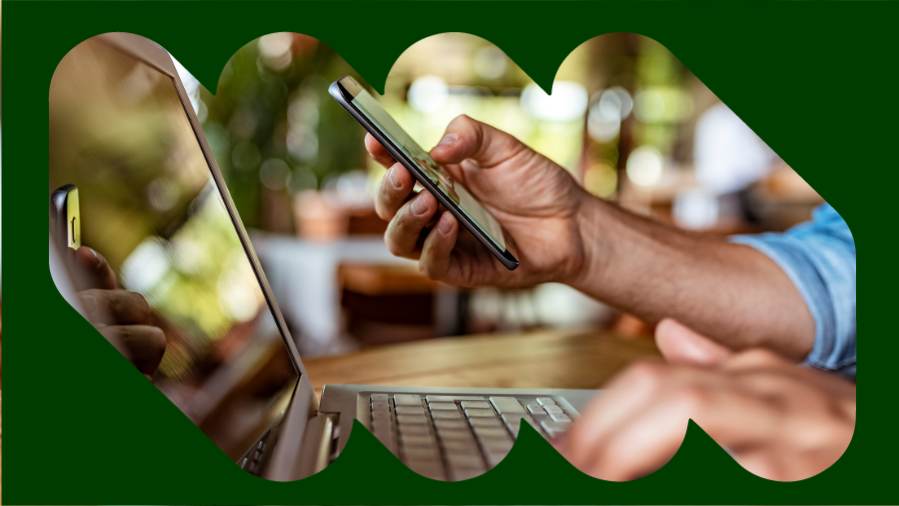 mão segurando celular na frente de notebook com fundo arborizado