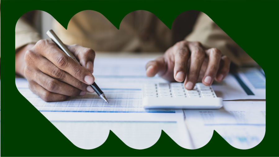 mão de homem negro escrevendo e digitando na calculadora. ao fundo, tabelas